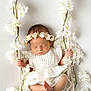 baby, sleeping, white_flowers, flower_crown, swing, crocheted_outfit, peaceful, infant, decorative, white_background, hand_grip, barefoot, portrait, cute, newborn, soft_lighting, indoor, closeup, child, adorable