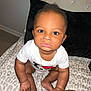 Vino is registered to the contest to win money with this photo: baby, infant, child, person, onesie, jewelry, gold_chain, bed, leopard_print, pillow, black_pillow, skin, hand, foot, face, eyes, expression, indoor, floor, curious