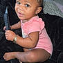 Nalani is registered to the contest to win money with this photo: baby, child, pink_onesie, comb, bracelet, black_blanket, indoor, cute, smiling, sitting, curly_hair, person, infant, skin, face, hand, foot, floor, decor, cozy