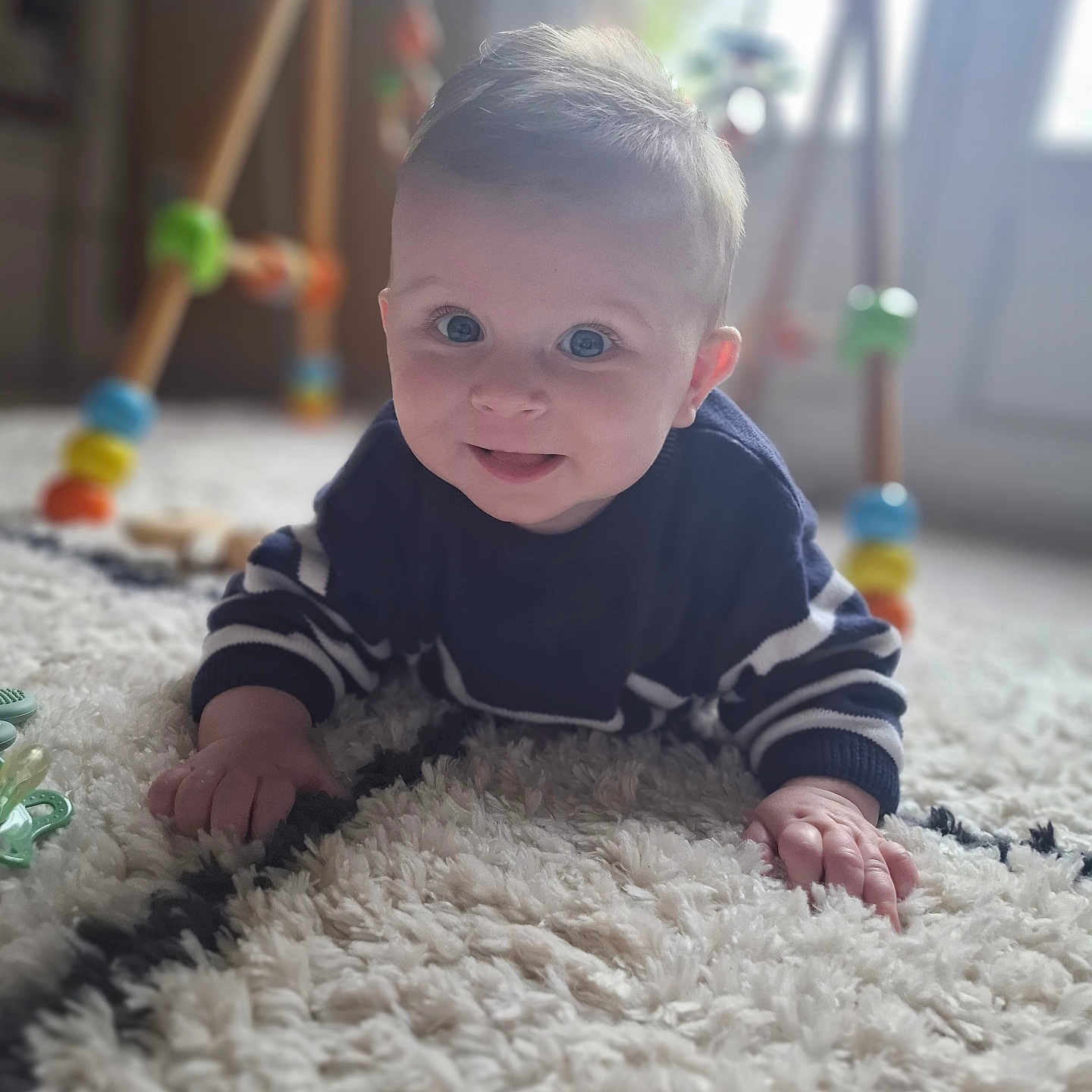 Julian a rejoint le concours — aidez-le/la à gagner de superbes lots ! baby, blue_eyes, carpet, child, colorful, crawling, cute, face, floor, hand, indoor, infant, person, playtime, rug, smiling, striped_sweater, toy, wooden_toy, young_child
