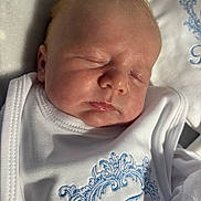 Tommy is registered to the contest to win money with this photo: baby, newborn, sleeping, face, infant, clothing, white_outfit, blue_embroidery, soft_light, peaceful, closeup, skin, head, portrait, resting, cute, child, indoors, texture, fabric