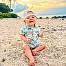 baby, beach, sand, sunset, ocean, palm_tree, child, smiling, cap, tropical_print, nature, outdoor, vacation, happy, sitting, footwear_free, sky, coast, toddler, casual_clothing