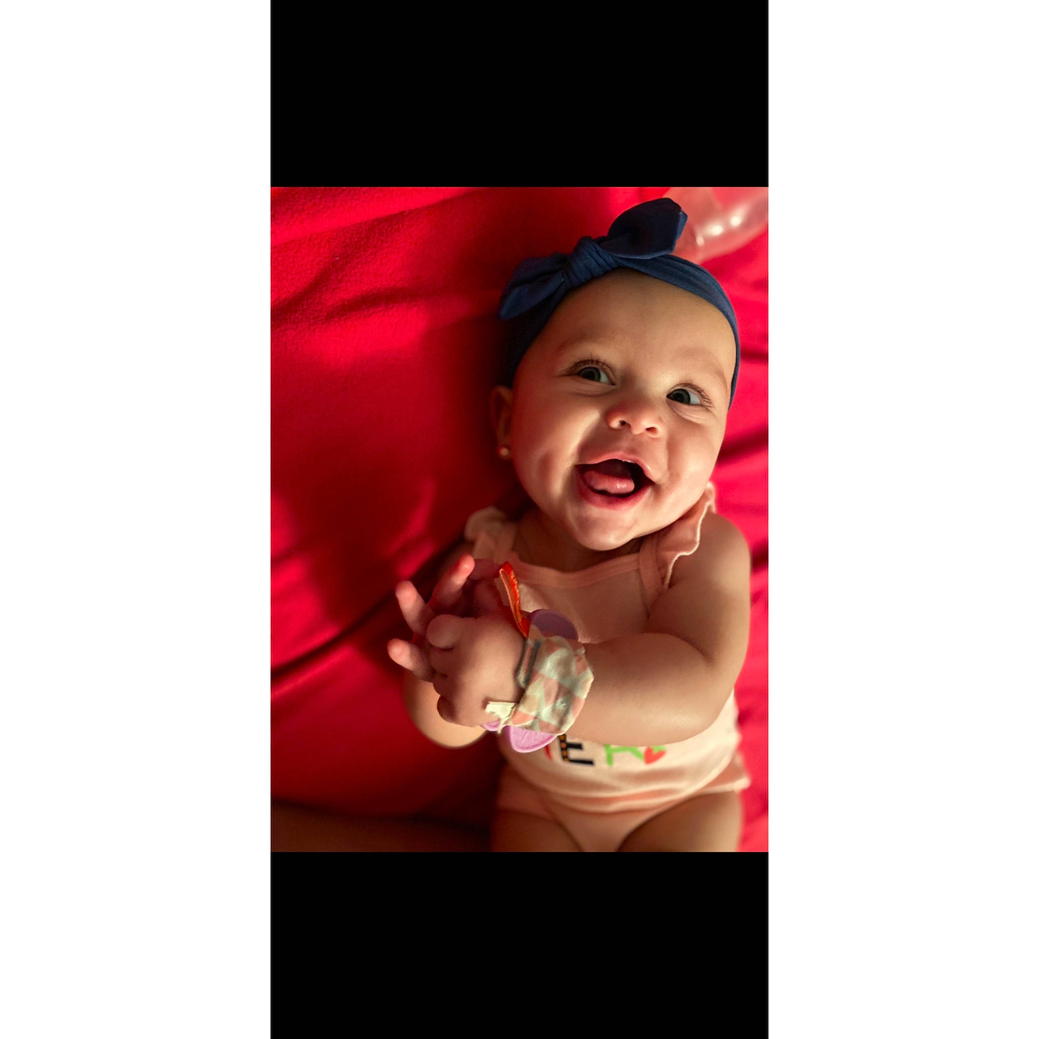 Gabriella is registered to the contest to win money with this photo: abdomen, baby, baby_laughing, baby_toddler_clothing, bonnet, child, costume_accessory, headwear, jewellery, long_sleeved_t_shirt, person, stomach, toddler, tongue, tooth