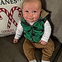 baby, infant, child, smiling, couch, green_vest, brown_pants, white_socks, holiday_pillow, candy_canes, indoor, face, cute, sitting, clothing, happy, portrait, cozy, home, young