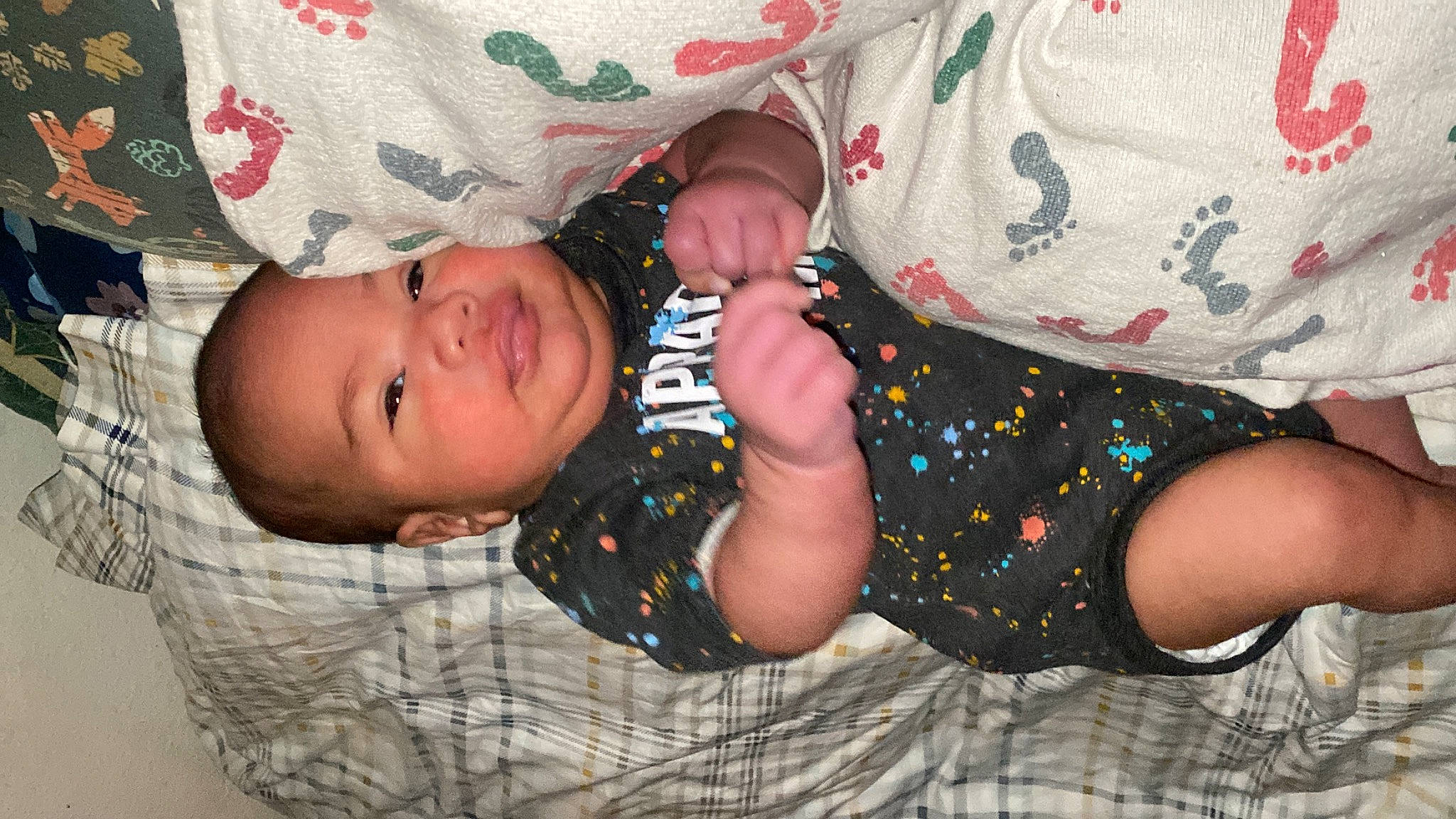 King is registered to the contest to win money with this photo: arm, baby, baby_products, baby_toddler_clothing, bedtime, cheek, child, comfort, facial_expression, hand, happy, linens, nail, pattern, person, room, sitting, skin, sleeve, smile