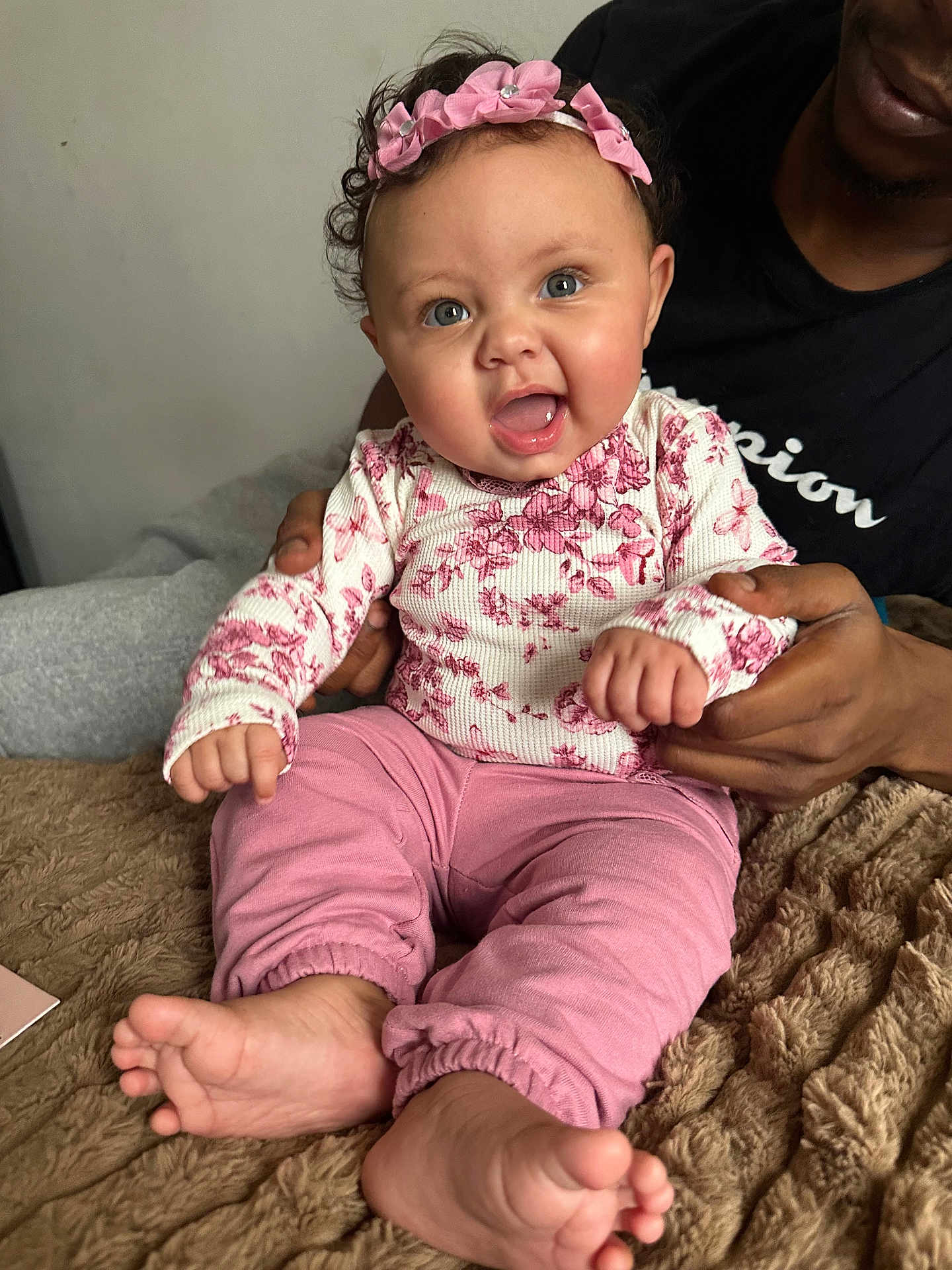 Maharmony joined the competition — help win amazing prizes! baby, child, infant, pink_clothing, headband, smiling, happy, blue_eyes, curly_hair, adult_hand, blanket, indoor, portrait, cute, sitting, cozy, support, family, person, closeup