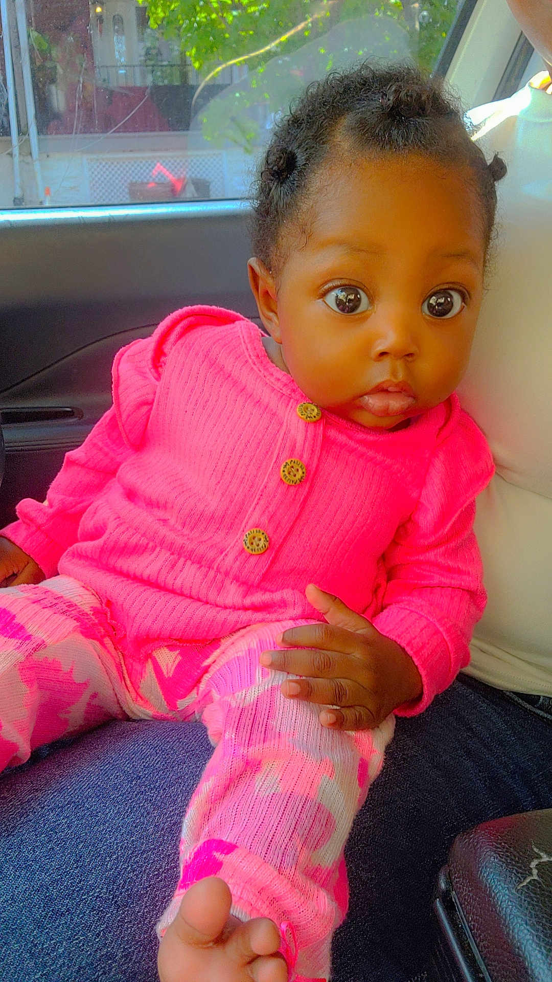Journey joined the competition — help win amazing prizes! baby, child, infant, pink_clothing, sitting, indoor, car_interior, curly_hair, wide_eyes, cute, portrait, hand, foot, buttoned_sweater, patterned_pants, young_child, person, casual, natural_light, expression
