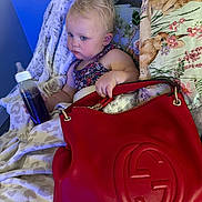 Maya joined the competition — help win amazing prizes! toddler, child, bottle, blanket, pillow, handbag, red_bag, couch, blue_lighting, indoor, furniture, baby, clothing, floral_pattern, sitting, face, person, cute, soft_texture, relaxed