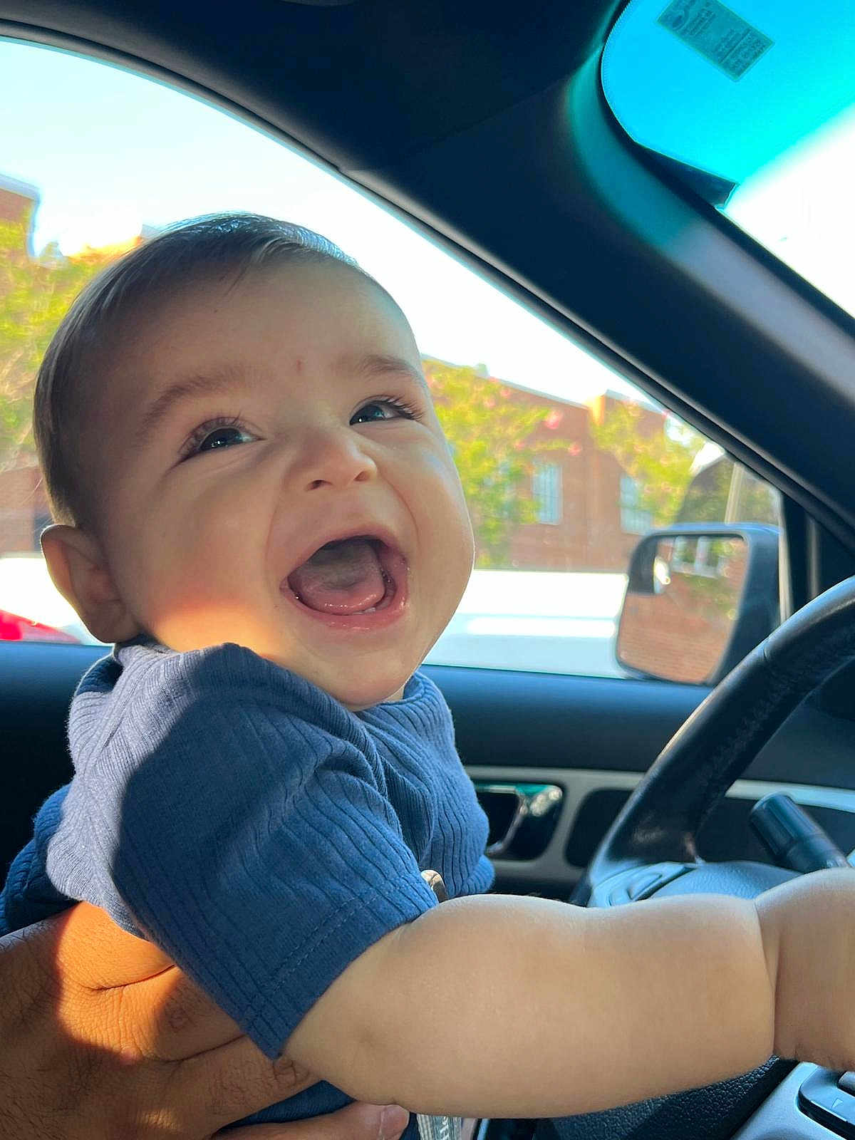 Matthias J joined the competition — help win amazing prizes! baby, child, smiling, laughing, blue_shirt, car_interior, hand, window, side_mirror, steering_wheel, sunlight, face, happy, person, infant, portrait, seat, automobile, candid, daylight