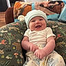 baby, smile, hat, pajamas, cushion, animal_pattern, indoor, living_room, happy, child, infant, person, cute, cozy, furniture, blanket, wood_floor, doorway, home, relaxed