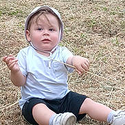 Kenzo a rejoint le concours — aidez-le/la à gagner de superbes lots ! toddler, child, sitting, grass, outdoor, hat, white_tshirt, black_shorts, stick, shoes, socks, plastic_chair, nature, curious, innocent, daylight, casual_clothing, young_child, ground, playful
