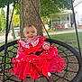child, toddler, swing, red_dress, outdoor, tree, rope_swing, grass, smiling, happy, play, park, nature, person, daylight, casual_clothing, house, porch, lawn_chairs, ground