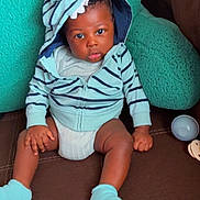 Isaiah joined the competition — help win amazing prizes! baby, child, hoodie, socks, couch, cushion, striped_clothing, indoor, seated, curious_expression, infant, hands, legs, face, person, soft_toys, brown, teal, comfortable, casual