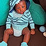 baby, child, hoodie, socks, couch, cushion, striped_clothing, indoor, seated, curious_expression, infant, hands, legs, face, person, soft_toys, brown, teal, comfortable, casual