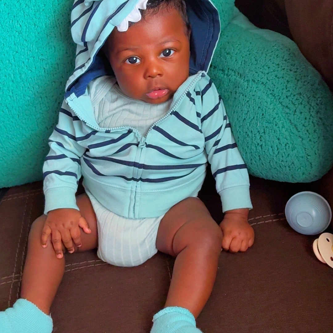 Isaiah joined the competition — help win amazing prizes! baby, brown, casual, child, comfortable, couch, curious_expression, cushion, face, hands, hoodie, indoor, infant, legs, person, seated, socks, soft_toys, striped_clothing, teal