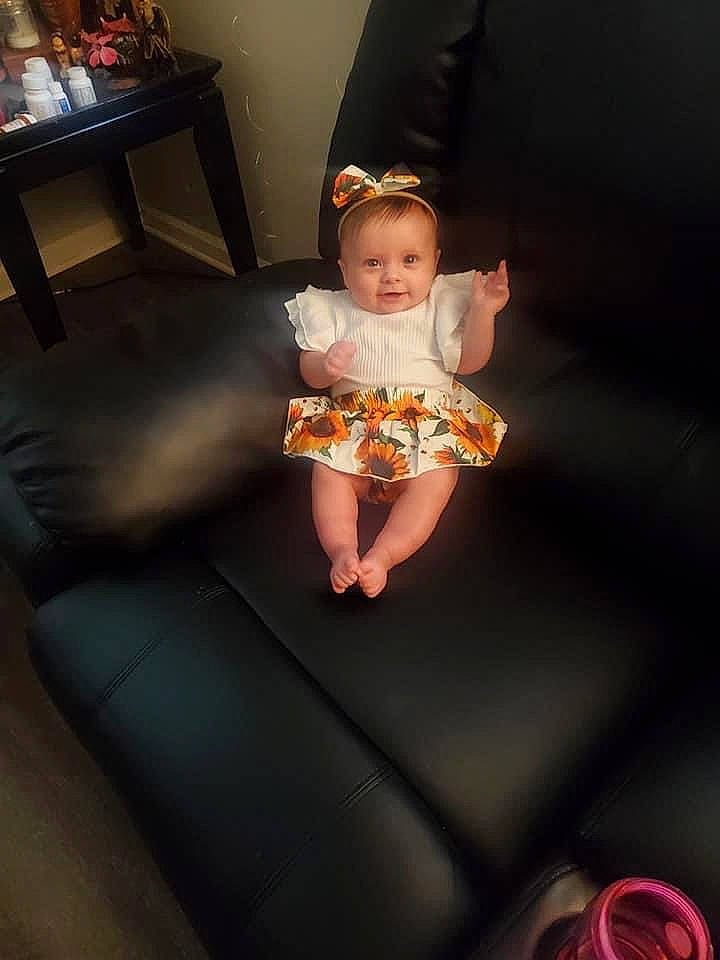 Lilly is registered to the contest to win money with this photo: baby, baby_toddler_clothing, child, dress, face, flash_photography, flooring, fun, hardwood, head, human_leg, magenta, person, pink, sandal, sitting, sock, table, thigh, toddler