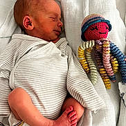 Augustin participe au concours pour gagner de l'argent avec cette photo : newborn, baby, sleeping, onesie, striped_clothing, blanket, crocheted_toy, octopus, colorful, soft, cute, infant, resting, child, foot, handmade_toy, smile, hat, cozy, bed