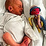 newborn, baby, sleeping, onesie, striped_clothing, blanket, crocheted_toy, octopus, colorful, soft, cute, infant, resting, child, foot, handmade_toy, smile, hat, cozy, bed