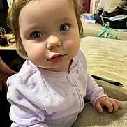 Athena joined the competition — help win amazing prizes! toddler, child, baby, face, blue_eyes, curly_hair, onesie, purple_clothing, indoor, couch, hand, furniture, person, portrait, curious_expression, home, cozy, soft_light, close_up, casual