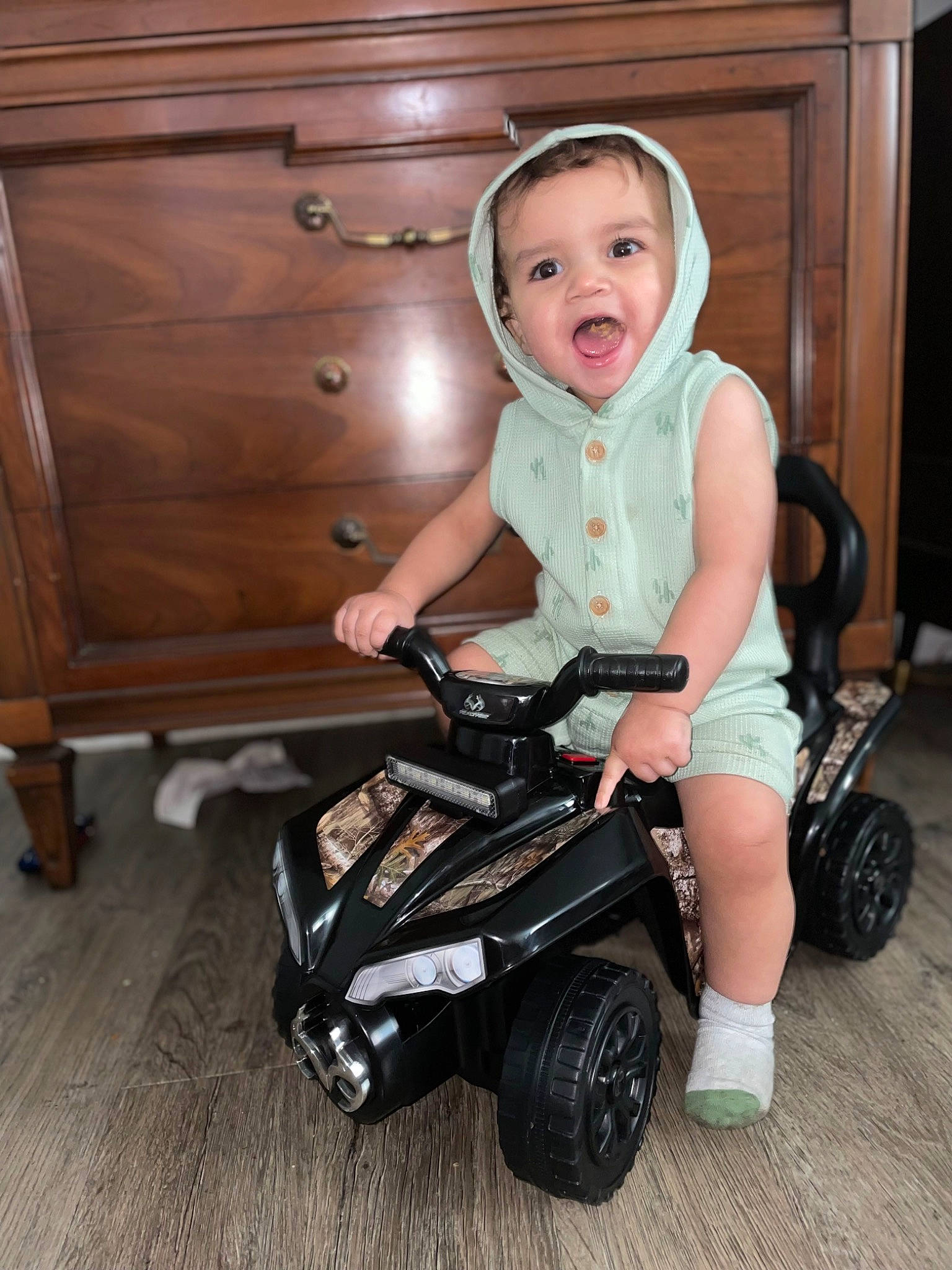 Alonzo is registered to the contest to win money with this photo: automotive_tire, baby_toddler_clothing, cabinetry, child, comfort, flash_photography, floor, flooring, fun, hardwood, person, riding_toy, rolling, sitting, smile, tire, toddler, toy, vehicle, wheel