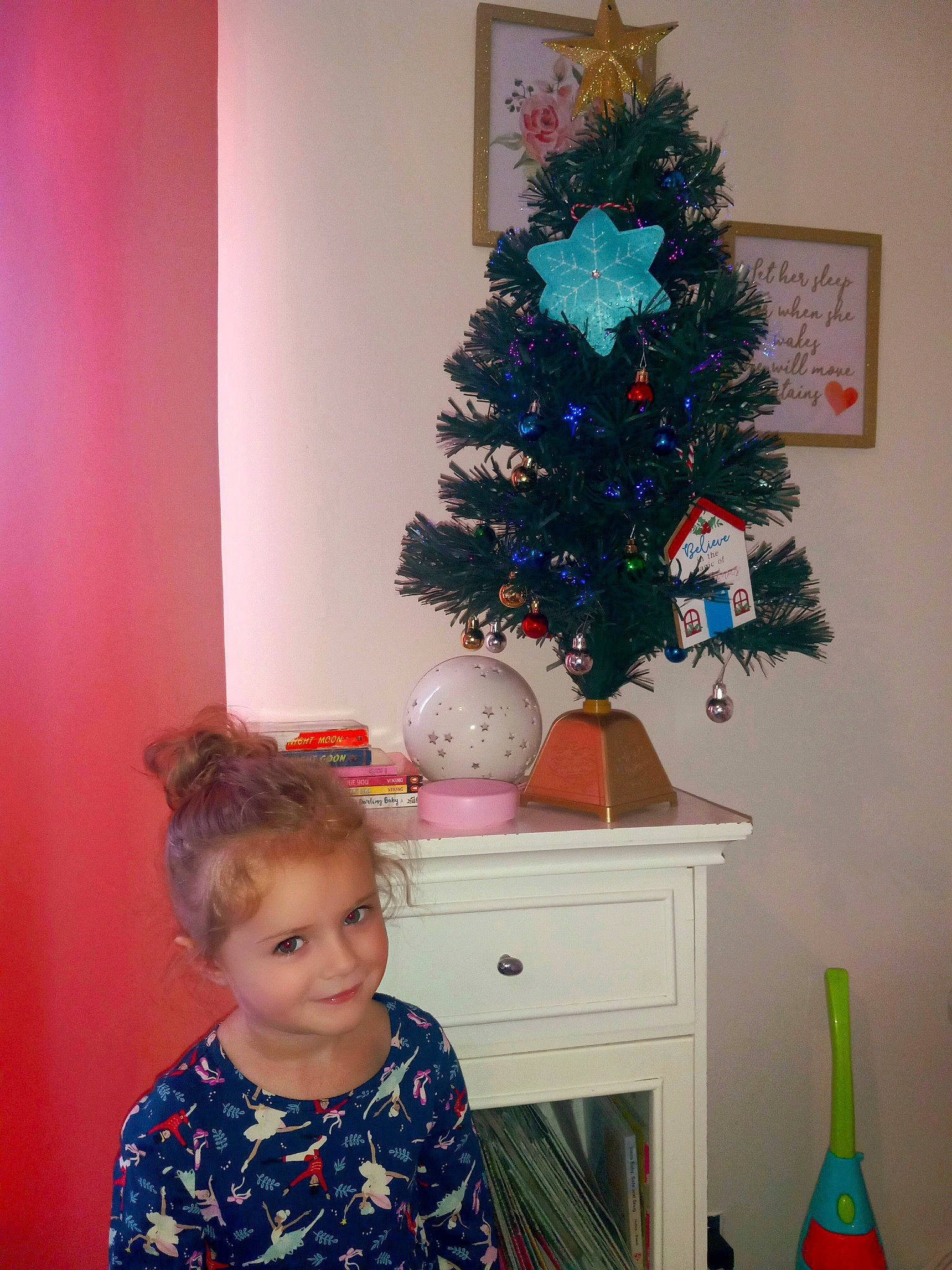 Annabelle is registered to the contest to win money with this photo: blue, christmas_decoration, christmas_ornament, christmas_tree, evergreen, green, holiday_ornament, joy, light, lighting, ornament, person, photograph, picture_frame, pink, plant, red, smile, toddler, tree