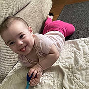 Norah is registered to the contest to win money with this photo: baby, child, tongue_out, toy, blanket, couch, carpet, floor, indoor, playful, smiling, cute, person, infant, clothing, pink_pants, white_shirt, happy, home, hand