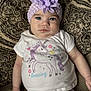 baby, child, infant, blue_eyes, headband, flower, unicorn, shirt, purple, white_shirt, patterned_couch, sitting, cute, portrait, clothing, daisy_shorts, hand, face, person, indoor