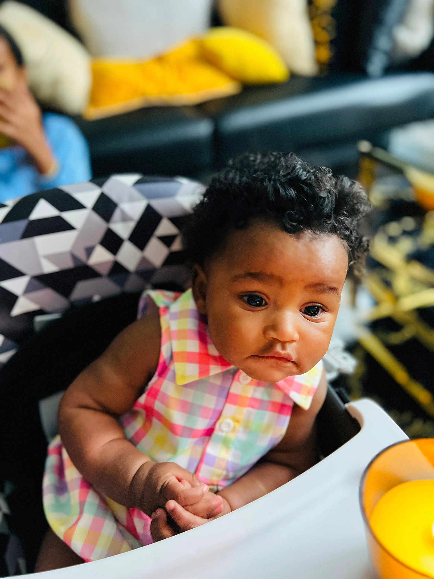 Jessie joined the competition — help win amazing prizes! baby, child, high_chair, curly_hair, colorful_clothing, indoor, person, face, hands, expression, seated, furniture, couch, pillow, background, soft_lighting, closeup, portrait, infant, cute