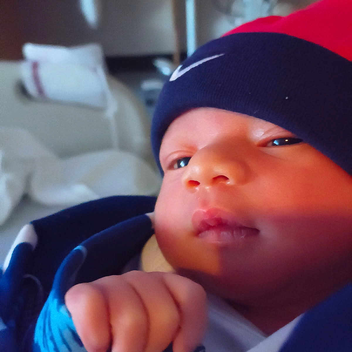 Tevon Xavier Brown is registered to the contest to win money with this photo: baby, blue_blanket, close_up, clothing, cozy, cute, expression, face, fist, hand, hat, indoors, infant, newborn, person, portrait, red_hat, skin, soft_lighting, wrapped