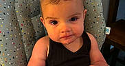 Kenzlee is registered to the contest to win money with this photo: toddler, child, baby, high_chair, pacifier, bows, hair, face, expression, clothing, sitting, indoor, table, food, hand, furniture, person, cute, curious, polka_dot