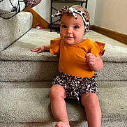 Kenzlee joined the competition — help win amazing prizes! baby, child, infant, carpet, stairs, headband, orange_clothing, leopard_print, sitting, indoors, smiling, person, portrait, cute, home_interior, shelf, bag, floor, wall, foot