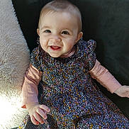 éléa a rejoint le concours — aidez-le/la à gagner de superbes lots ! baby, black_background, blanket, cheerful, child, cute, dress, face, floral_pattern, happy, indoor, infant, long_sleeve, person, pink, portrait, sitting, smiling, soft_texture, young