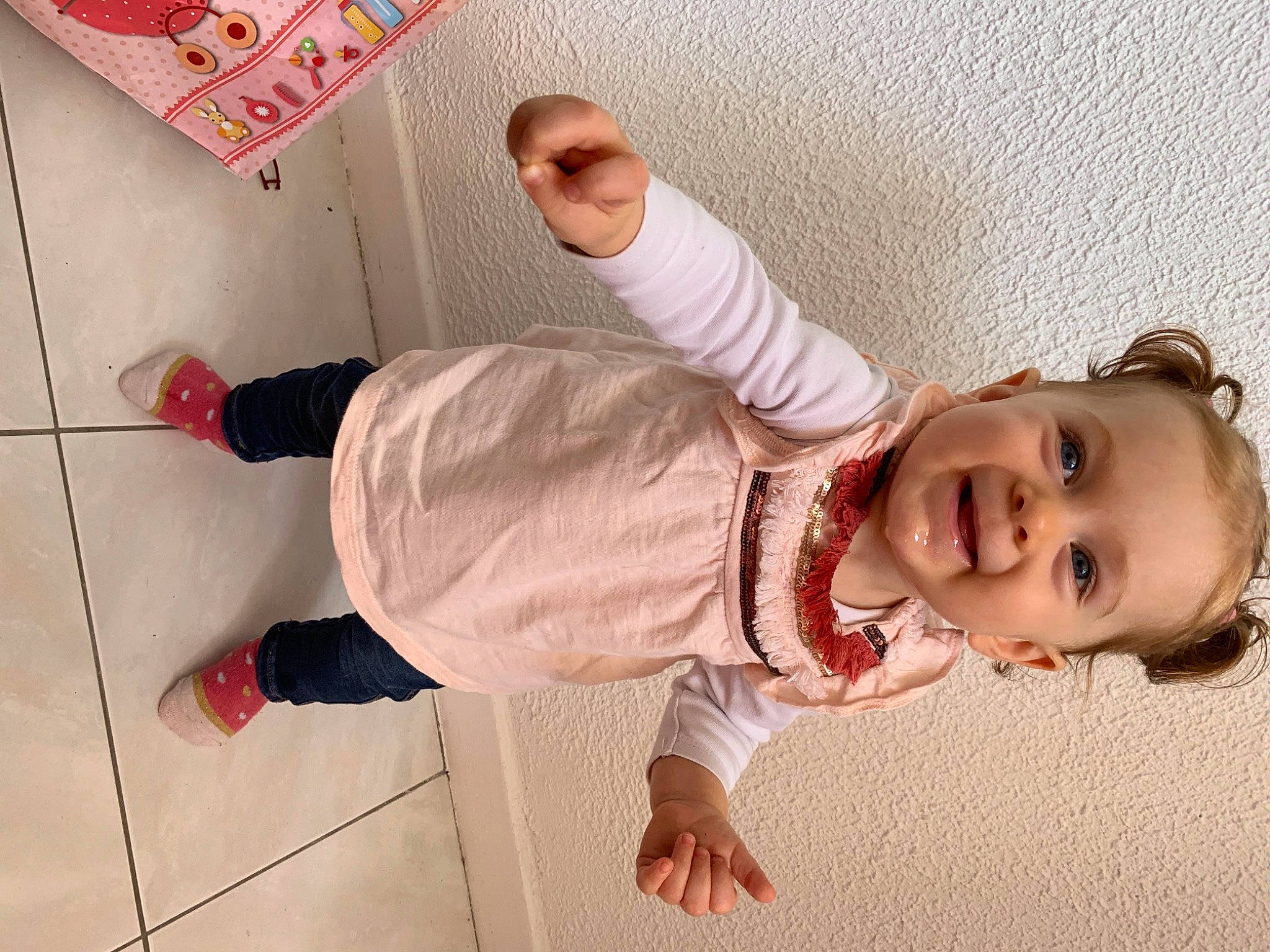 Ilana a rejoint le concours — aidez-le/la à gagner de superbes lots ! baby, baby_toddler_clothing, child, facial_expression, finger, floor, flooring, fun, hand, happy, joint, leg, pattern, person, pink, red, skin, sleeve, smile, toddler