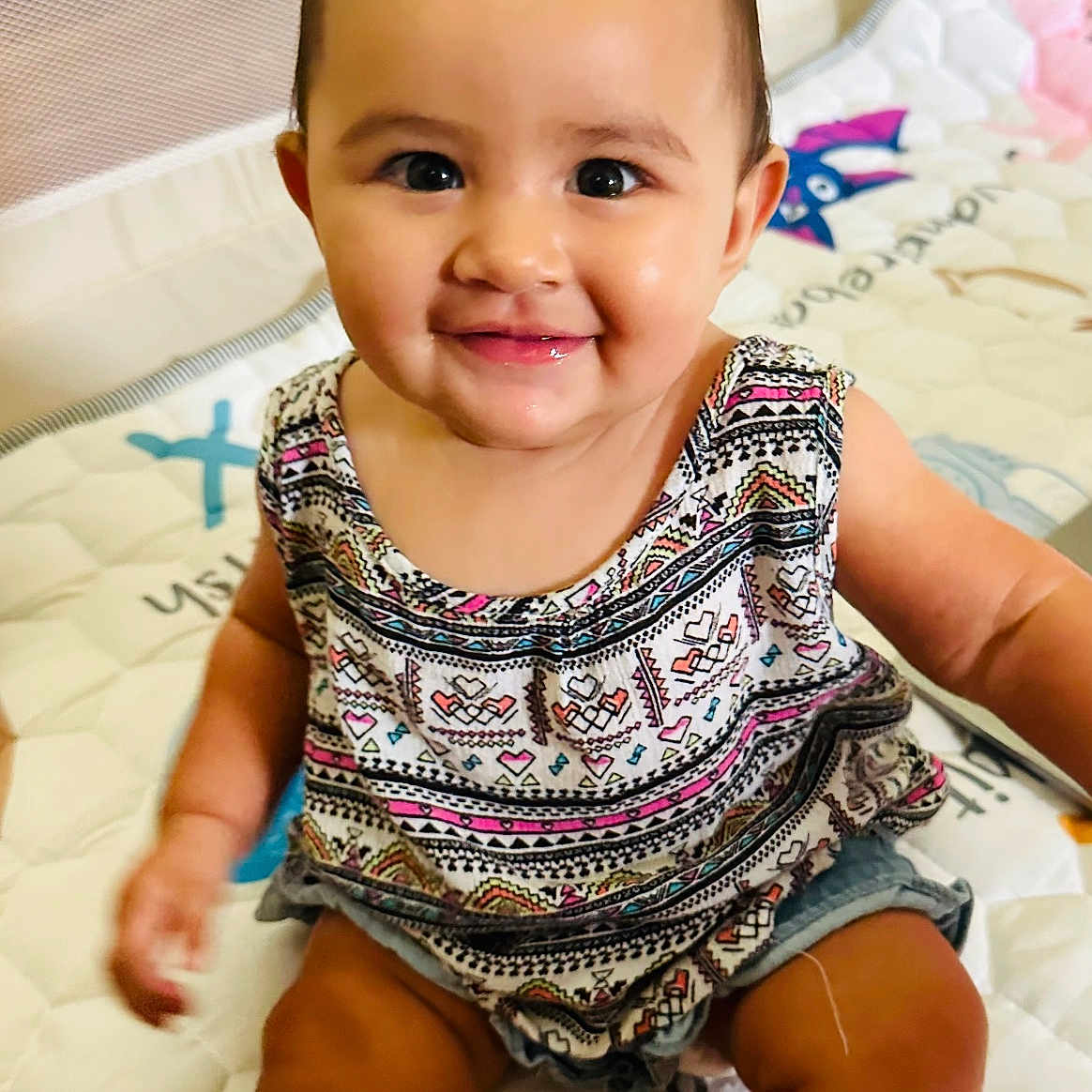 Shiloh is registered to the contest to win money with this photo: baby, child, smiling, sitting, indoor, playmat, patterned_clothing, cute, happy, portrait, infant, cheerful, young_child, skin, face, head, short_hair, person, baby_toddler, colorful