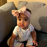 River joined the competition — help win amazing prizes! baby, child, headband, bow, onesie, couch, sofa, sitting, indoors, portrait, eyes, face, hands, feet, toes, expression, living_room, soft_lighting, adorable, curious