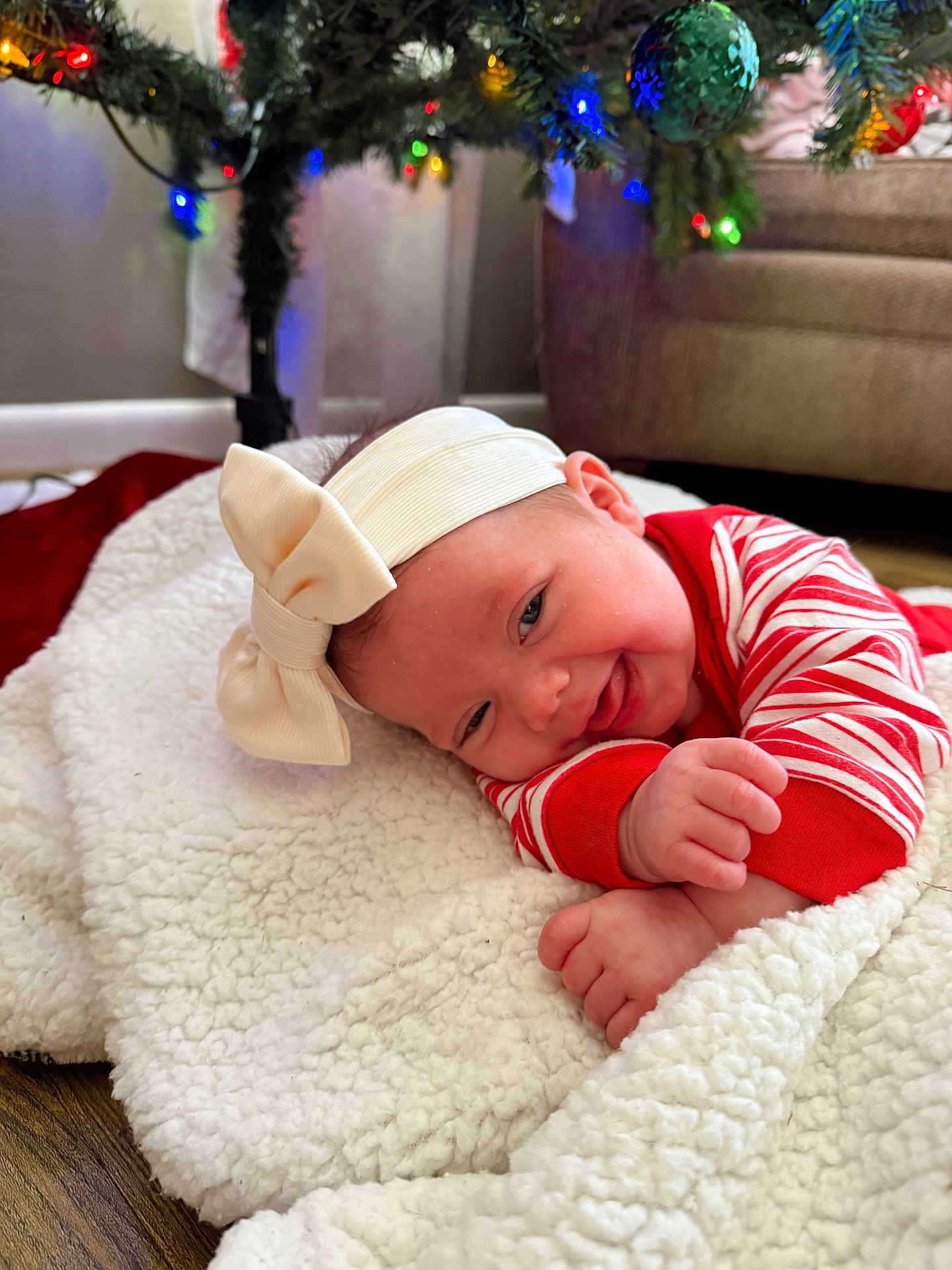 Caylin is registered to the contest to win money with this photo: baby, headband, bow, blanket, christmas_tree, christmas_lights, pajamas, red, white, smiling, indoor, floor, decorations, holiday, festive, cute, infant, toddler, happy, cozy