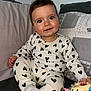 baby, child, heart_pattern, pajamas, toy, couch, pillow, indoor, smile, cute, infant, sitting, cozy, soft_lighting, portrait, happy, playful, young_child, comfortable, home
