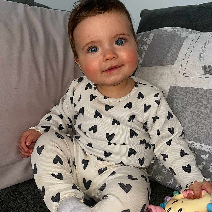 Thea is registered to the contest to win money with this photo: baby, child, comfortable, couch, cozy, cute, happy, heart_pattern, home, indoor, infant, pajamas, pillow, playful, portrait, sitting, smile, soft_lighting, toy, young_child