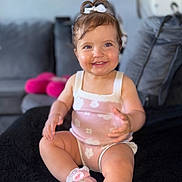 Thea is registered to the contest to win money with this photo: toddler, child, smiling, pink_outfit, pink_shoes, bow, sitting, indoor, couch, cushion, happy, baby, short_hair, cute, face, person, footwear, sock, living_room, portrait