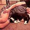person, dog, sleeping, cuddling, carpet, indoor, home, nap, relaxed, black_and_white_dog, fluffy, pet, human, lying_down, shorts, shirt, plaid, cozy, living_room, portrait