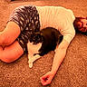 cat, black_and_white_cat, person, lying_down, carpet, indoor, living_room, pet, human_animal_bond, short_hair, white_shirt, patterned_shorts, warm_lighting, portrait, funny_pose, relaxed, floor, whiskers, feline, domestic_scene