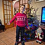 Gabriel a rejoint le concours — aidez-le/la à gagner de superbes lots ! child, boy, christmas_tree, holiday, indoor, festive, sweater, reindeer_pattern, smiling, home, decorations, santa_figure, living_room, wooden_door, tiled_floor, television, person, celebration, winter_clothing, happy