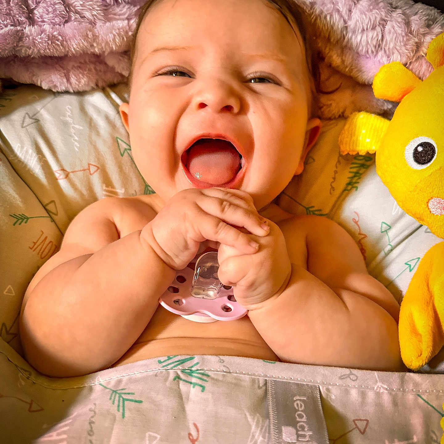 Delaney is registered to the contest to win money with this photo: baby, bed, blanket, child, comfort, cozy, cute, face, hands, happy, indoors, infant, joy, laughing, pacifier, playful, plush_toy, smiling, soft, yellow