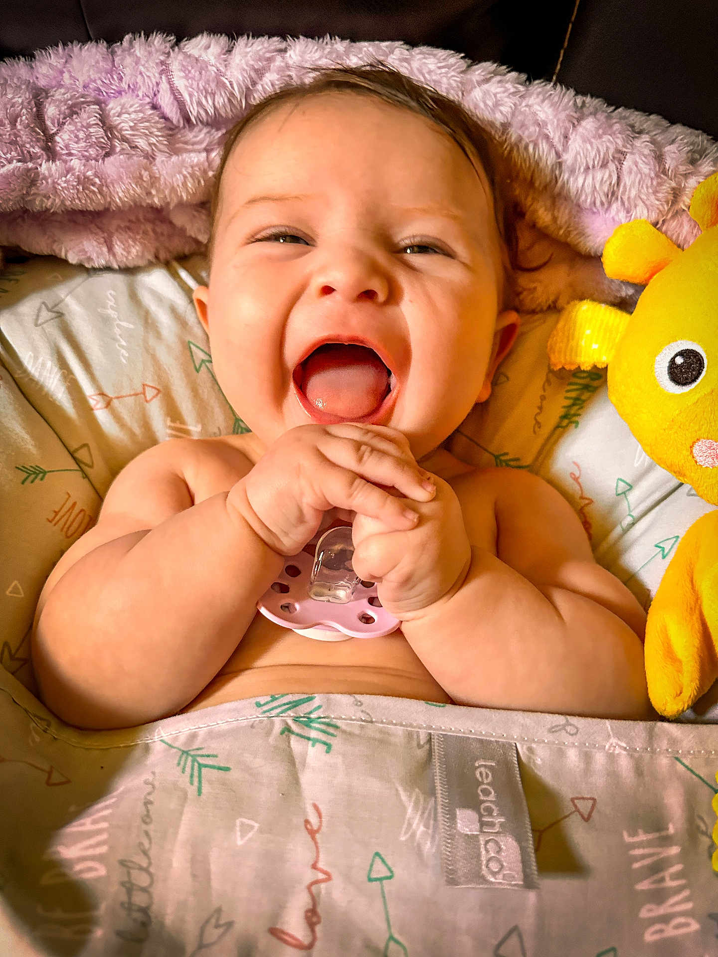 Delaney is registered to the contest to win money with this photo: baby, laughing, pacifier, blanket, plush_toy, yellow, happy, child, infant, cute, smiling, hands, face, cozy, bed, soft, comfort, playful, joy, indoors