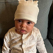 Soan participe au concours pour gagner de l'argent avec cette photo : baby, child, infant, hat, onesie, dinosaur_pattern, couch, gray_couch, sitting, tongue_out, cute, indoors, soft_lighting, face, hand, clothing, buttoned_onesie, headwear, expression, portrait
