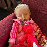 Delilah joined the competition — help win amazing prizes! baby, sleeping, pink_jacket, pacifier, plush_toy, red_plush, maroon_chair, blanket, soft_lighting, indoor, child, cute, peaceful, cozy, resting, clothing, infant, adorable, face, nap