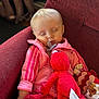 baby, sleeping, pink_jacket, pacifier, plush_toy, red_plush, maroon_chair, blanket, soft_lighting, indoor, child, cute, peaceful, cozy, resting, clothing, infant, adorable, face, nap