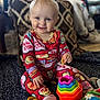 baby, child, pajamas, smiling, toy, colorful, indoor, blanket, face, sitting, cute, playtime, snack, hand, footwear, person, patterned_clothing, happy, home, infant