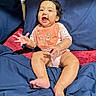 Mahi is registered to the contest to win money with this photo: baby, bed, bib, blanket, blue_blanket, child, clothing, cute, face, foot, hand, happy, indoors, infant, person, portrait, red_blanket, sitting, smiling, young
