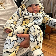 Lennox joined the competition — help win amazing prizes! baby, infant, child, onesie, hat, elephant_pattern, hand, person, indoor, wood_floor, jacket, gold_chains, holding, cute, warm_clothing, face, eyes, expression, casual, portrait